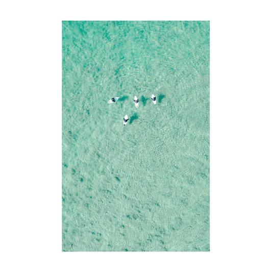 Aerial view of four paddleboarders floating over clear turquoise waters at North Avoca Beach, NSW.