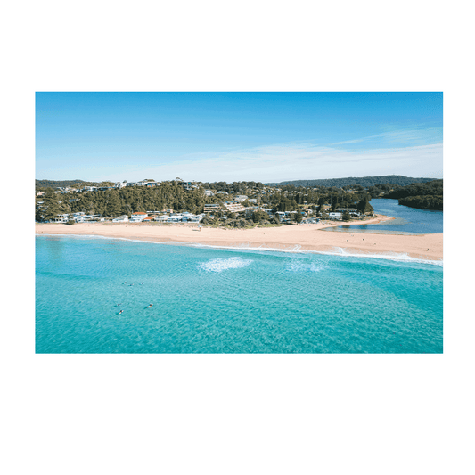 Aerial view of North Avoca Beach, NSW, showcasing golden sand, turquoise waters, and the winding lagoon with surfers enjoying the waves.