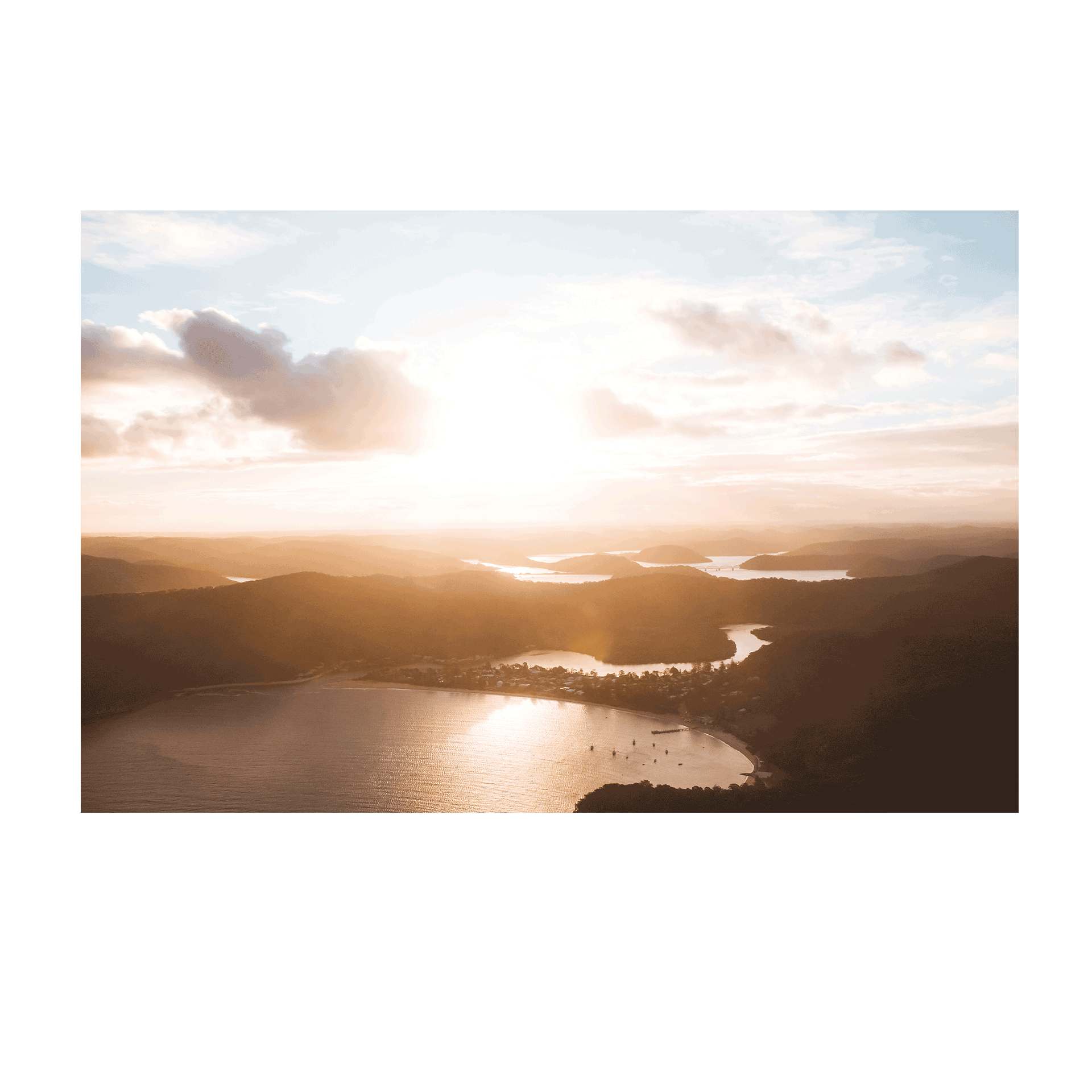 Aerial view of Patonga, NSW, bathed in golden sunset light, with rolling hills and shimmering waterways.