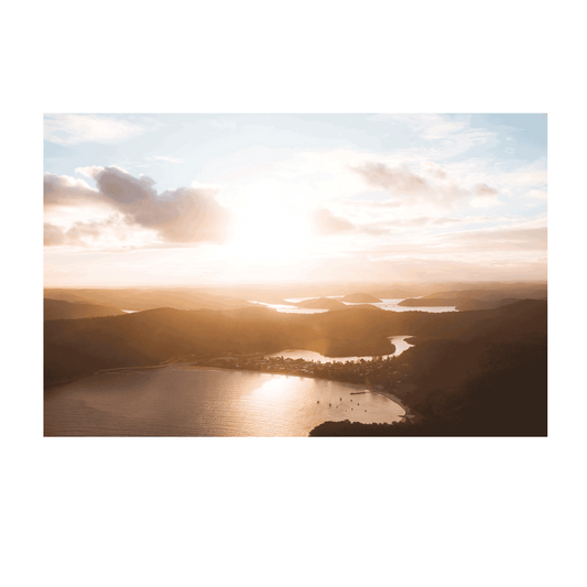 Aerial view of Patonga, NSW, bathed in golden sunset light, with rolling hills and shimmering waterways.