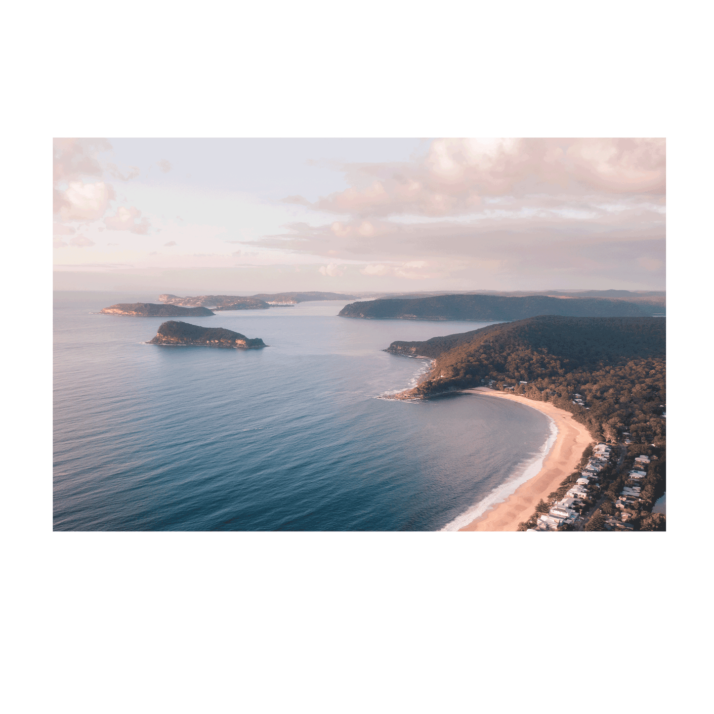 A breathtaking aerial view of Pearl Beach and Lion Island, NSW, with golden sunlight casting a warm glow over the coastline and tranquil blue waters.