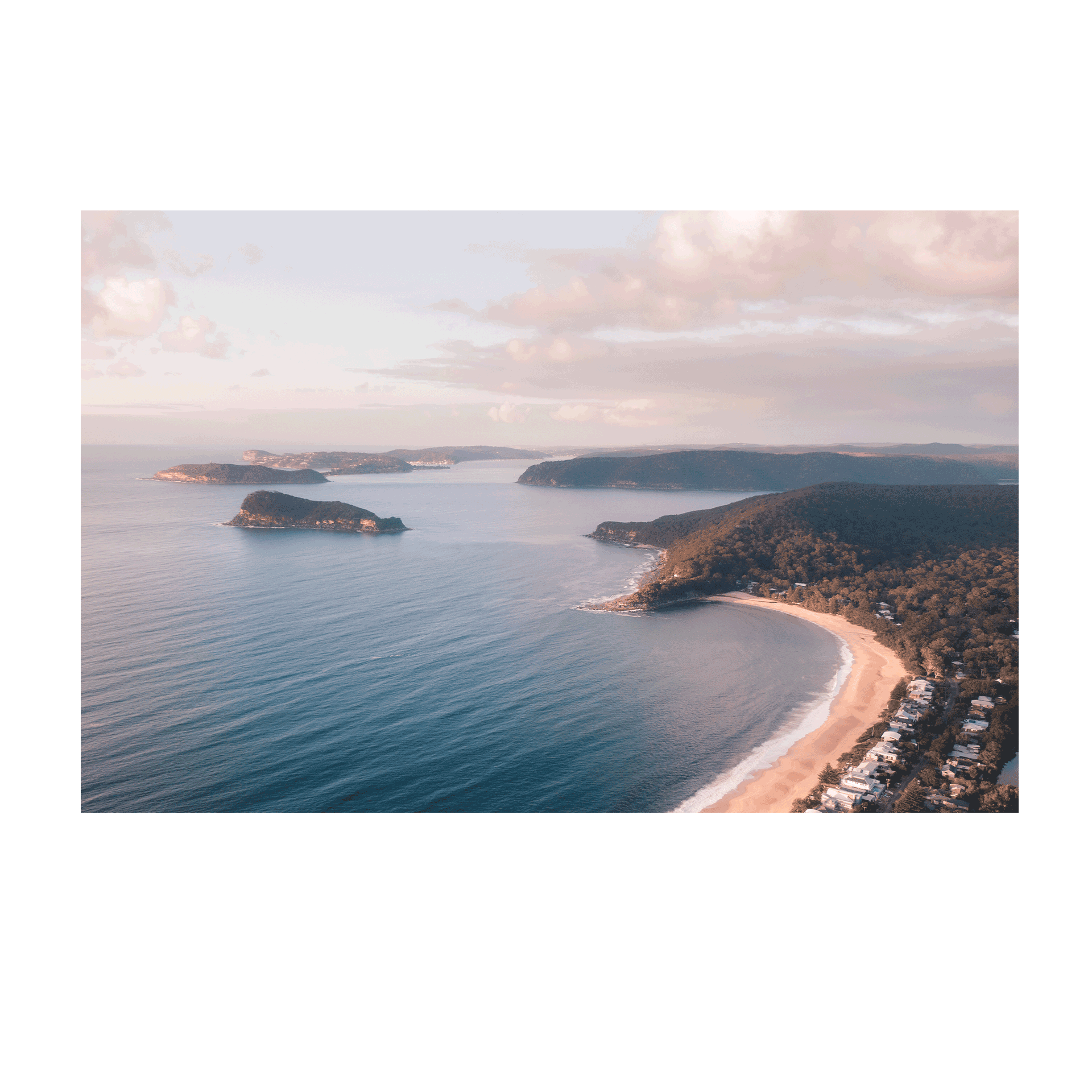 A breathtaking aerial view of Pearl Beach and Lion Island, NSW, with golden sunlight casting a warm glow over the coastline and tranquil blue waters.