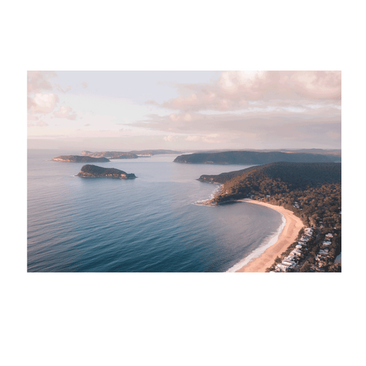 A breathtaking aerial view of Pearl Beach and Lion Island, NSW, with golden sunlight casting a warm glow over the coastline and tranquil blue waters.