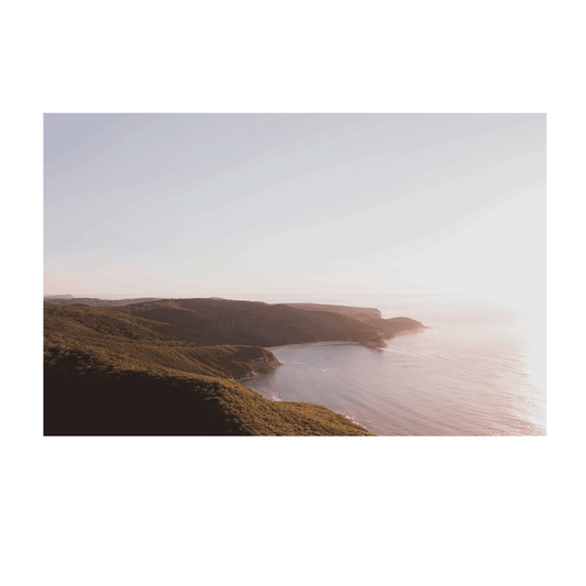 An aerial coastal view of Putty Beach, Central Coast, bathed in soft golden light, with lush green headlands and deep blue waters meeting under a gentle morning haze.