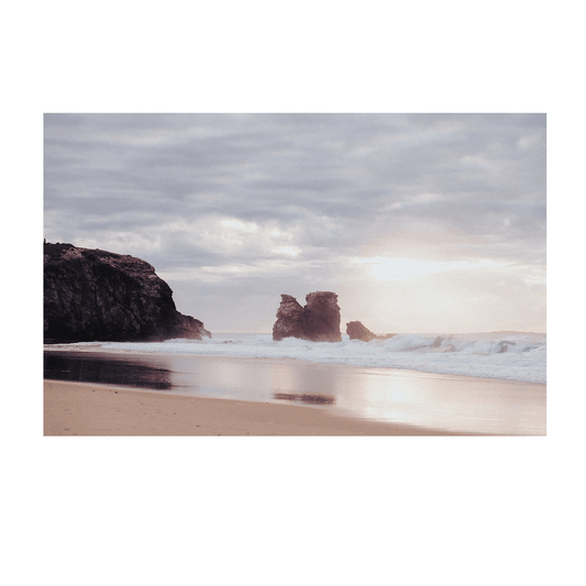 A serene scene of Red Rock, NSW, with dramatic rock formations and gentle waves crashing on the shore, reflecting the soft hues of the sky.
