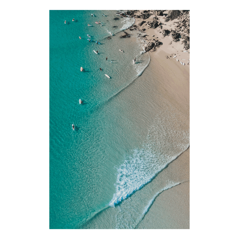 Aerial view of Scotts Head Beach, NSW, showcasing turquoise waters, gentle waves, and surfers along the sandy shoreline on a serene winter day.