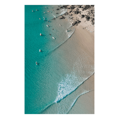 Aerial view of Scotts Head Beach, NSW, showcasing turquoise waters, gentle waves, and surfers along the sandy shoreline on a serene winter day.