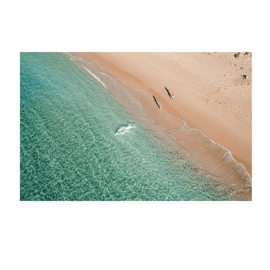 An aerial view of Shelly Beach, Central Coast, featuring two people walking along the golden shoreline, their shadows stretching across the sand as turquoise waters meet the shore.