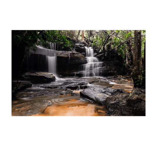 A stunning waterfall scene at Somersby Falls, Central Coast, with cascading water flowing over rugged rock formations, surrounded by lush green rainforest.
