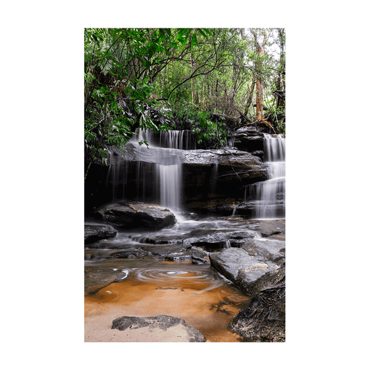 A tranquil waterfall scene at Somersby Falls, Central Coast, where water cascades over rugged rocks, surrounded by lush rainforest greenery.