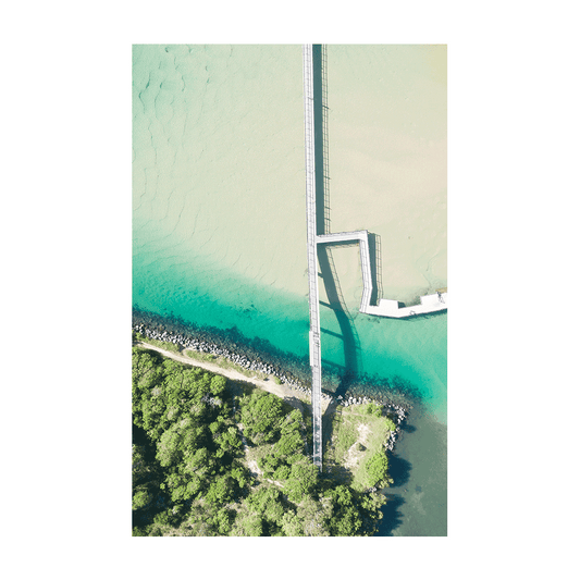 A stunning aerial view of South West Rocks, NSW, featuring a long jetty stretching across turquoise waters and lush greenery.