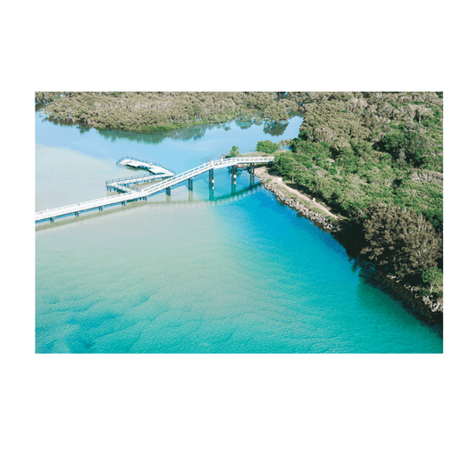 A stunning aerial print of South West Rocks, NSW, featuring a charming wooden bridge crossing over vibrant turquoise waters and lush greenery.