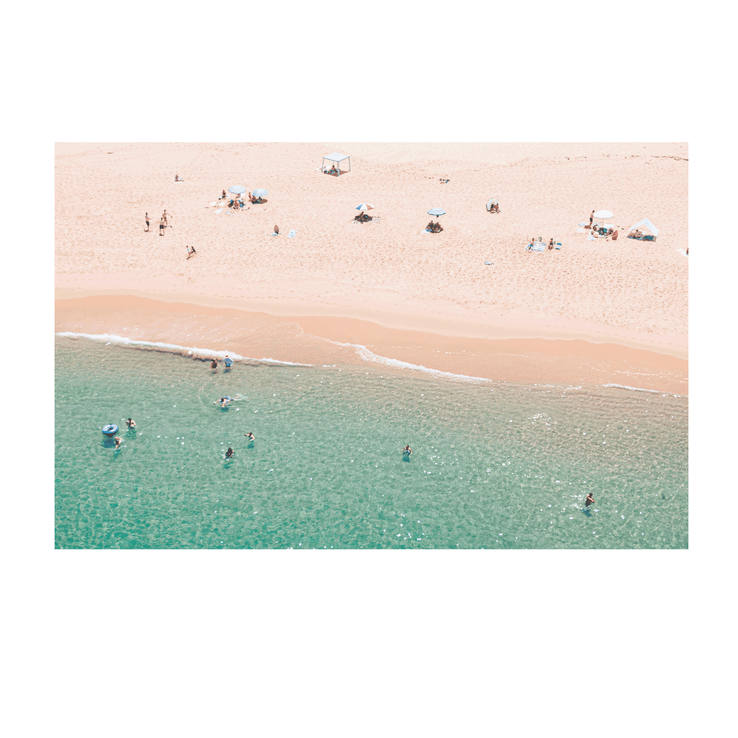 An aerial view of Spoon Bay, Central Coast, with beachgoers lounging under umbrellas on golden sands while swimmers enjoy the crystal-clear turquoise waters.