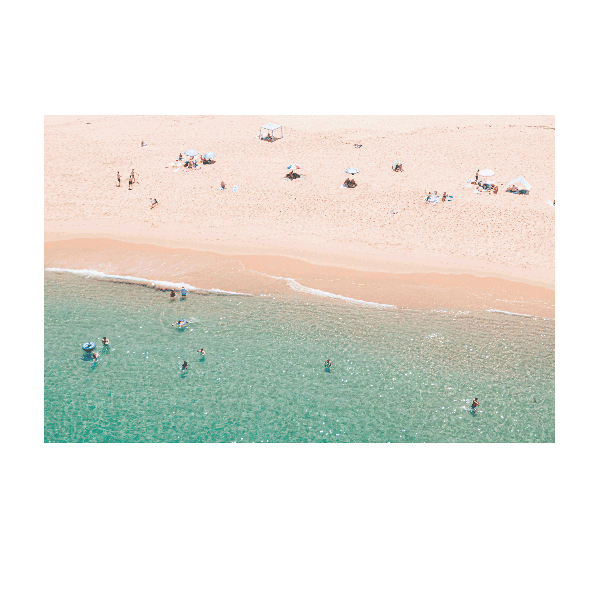 An aerial view of Spoon Bay, Central Coast, with beachgoers lounging under umbrellas on golden sands while swimmers enjoy the crystal-clear turquoise waters.