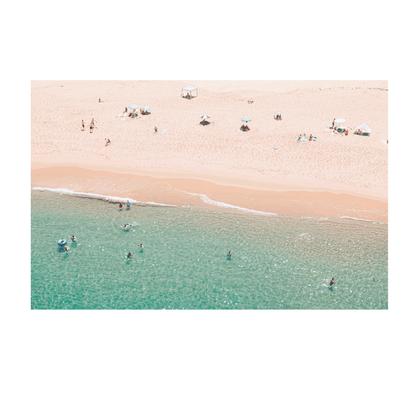 An aerial view of Spoon Bay, Central Coast, with beachgoers lounging under umbrellas on golden sands while swimmers enjoy the crystal-clear turquoise waters.