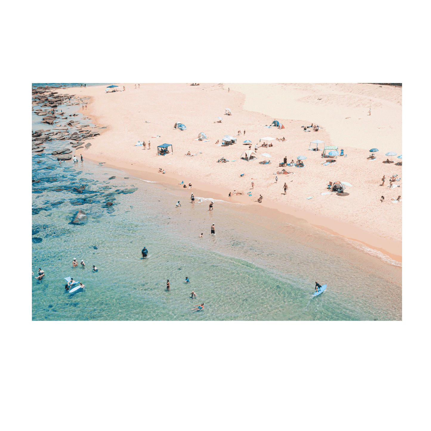 An aerial view of Spoon Bay, Central Coast, filled with beachgoers enjoying golden sands, scattered umbrellas, and turquoise waters on a perfect summer day.