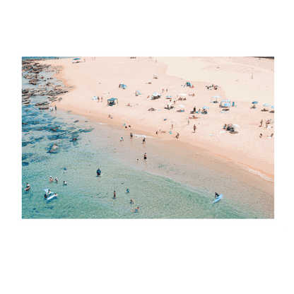 An aerial view of Spoon Bay, Central Coast, filled with beachgoers enjoying golden sands, scattered umbrellas, and turquoise waters on a perfect summer day.