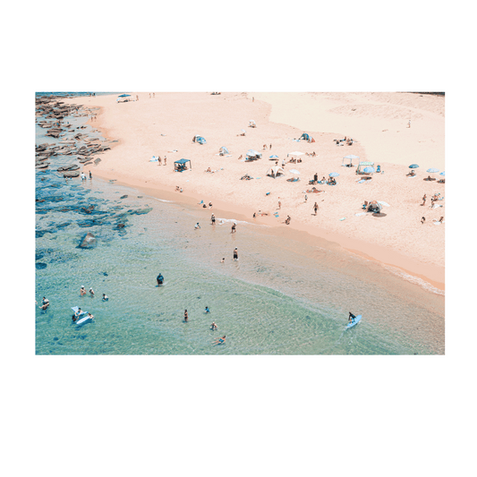 An aerial view of Spoon Bay, Central Coast, filled with beachgoers enjoying golden sands, scattered umbrellas, and turquoise waters on a perfect summer day.