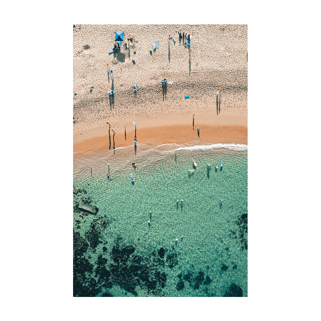 An aerial view of Spoon Bay, Central Coast, featuring beachgoers enjoying crystal-clear turquoise waters and golden sands under bright summer sunshine.