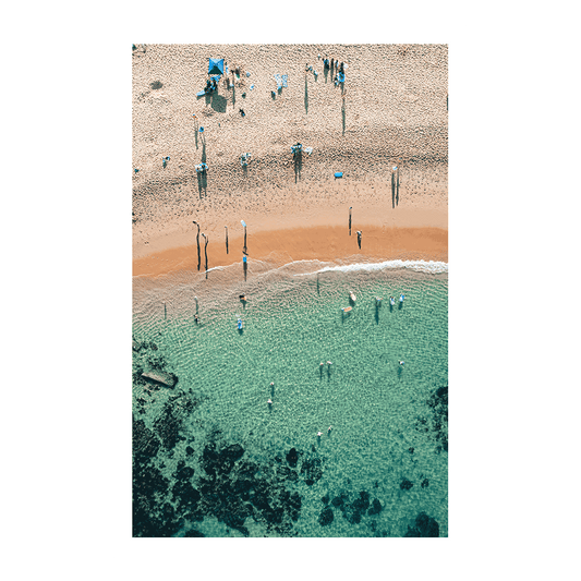 An aerial view of Spoon Bay, Central Coast, featuring beachgoers enjoying crystal-clear turquoise waters and golden sands under bright summer sunshine.