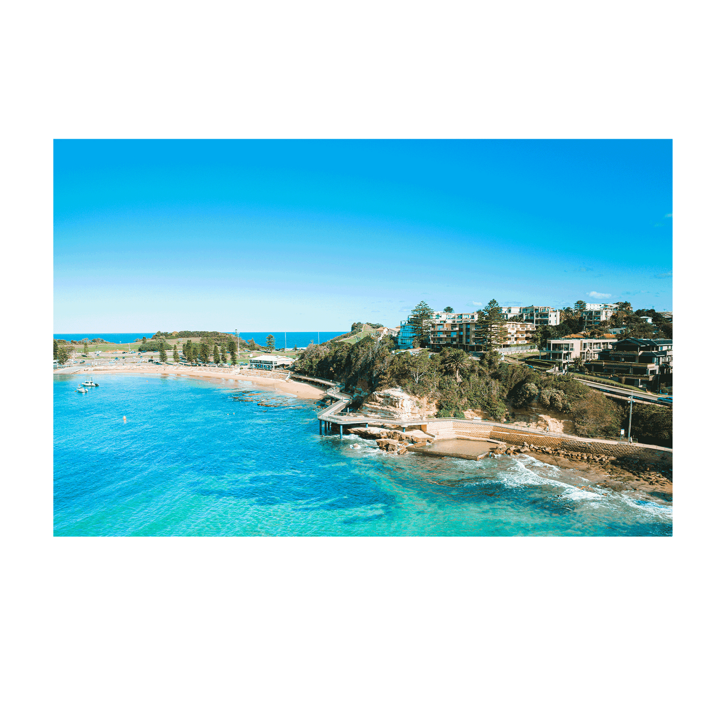 An aerial view of Terrigal Beach, NSW, showcasing the vibrant blue ocean, a winding coastal walkway, and the picturesque beachside community.
