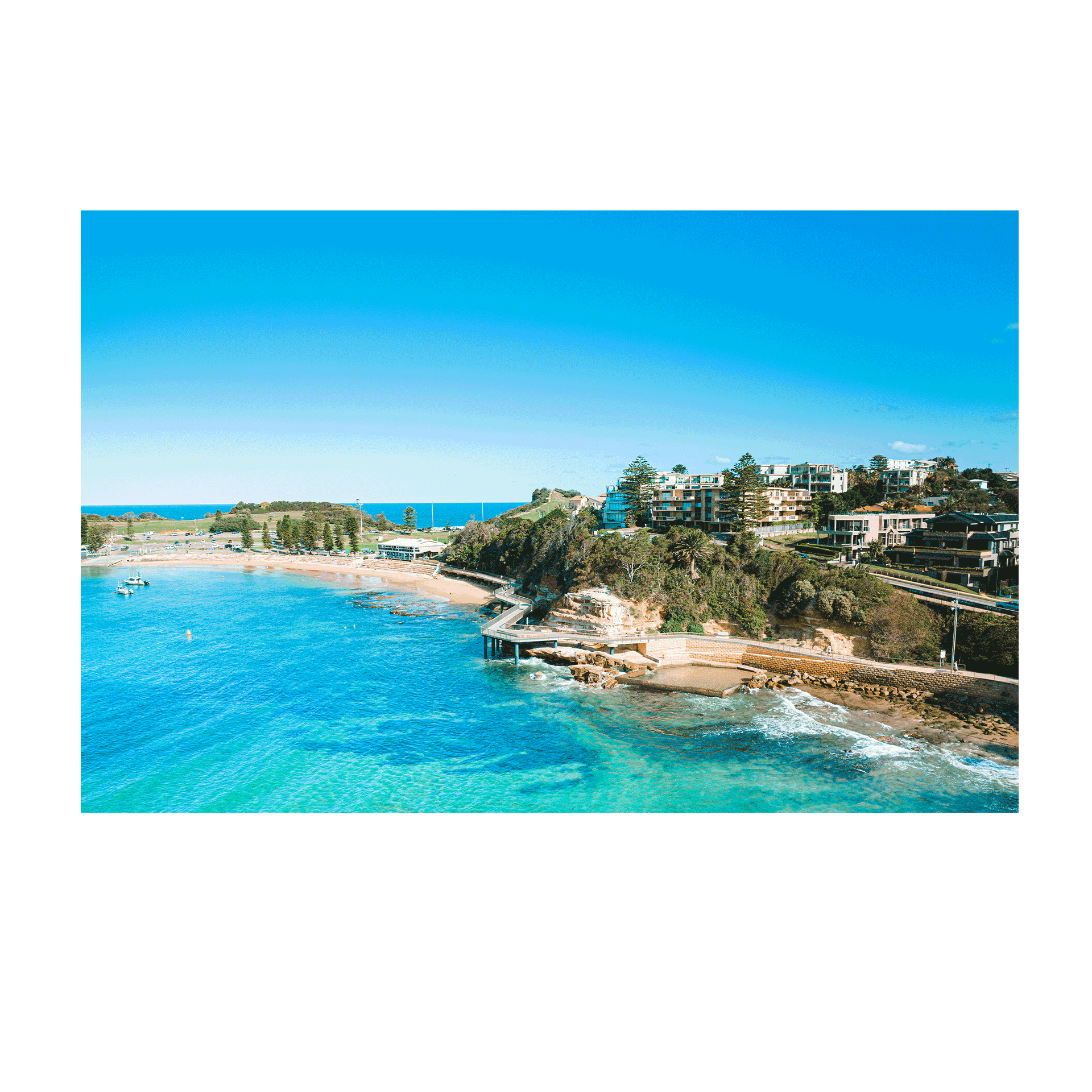 An aerial view of Terrigal Beach, NSW, showcasing the vibrant blue ocean, a winding coastal walkway, and the picturesque beachside community.
