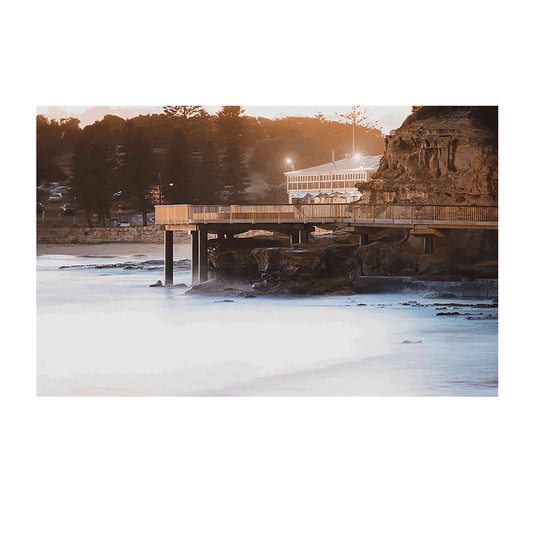 A moody coastal scene at Terrigal Beach, NSW, featuring the boardwalk stretching over misty waters at dusk, bathed in soft golden light.