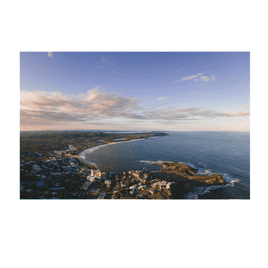 A breathtaking aerial view of Terrigal Beach, NSW, at golden hour, showcasing a vast ocean, rolling hills, and a pastel-hued sky with soft clouds.