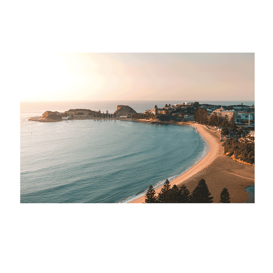 An aerial view of Terrigal Beach, NSW, at sunrise, with golden light casting a warm glow over the sand, ocean, and surrounding coastal landscape.