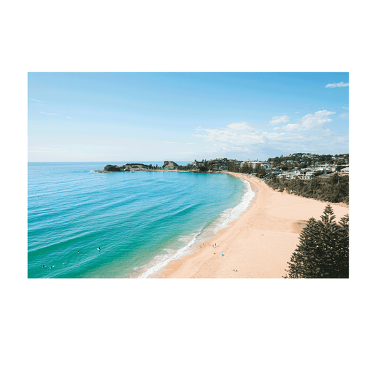 An aerial view of Terrigal Beach, NSW, showing golden sand, turquoise ocean waves, and swimmers enjoying the water on a sunny day.
