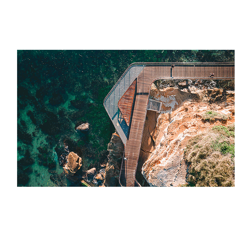 An aerial view of the Terrigal boardwalk, showing its elegant curves over the rocky coastline with turquoise ocean waters below.