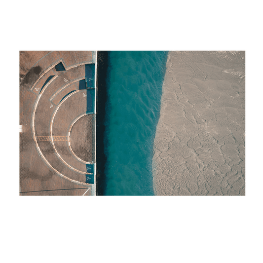 A striking aerial print of The Entrance, NSW, showcasing a curved architectural design meeting the shoreline, with deep blue waters and textured sand patterns.