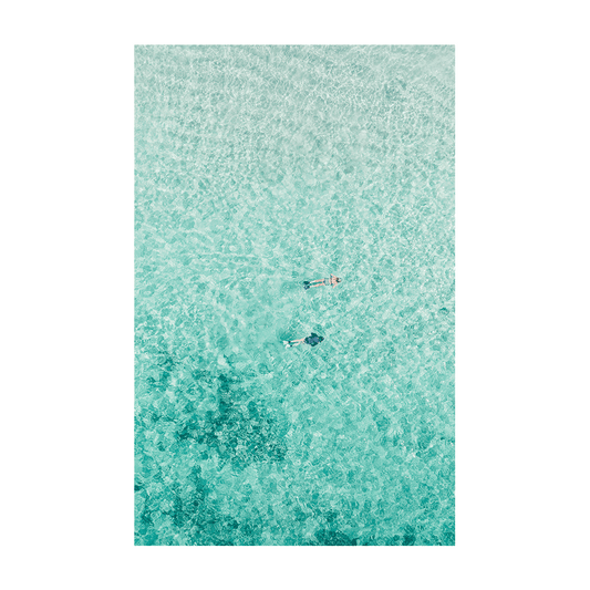 A serene aerial print of Toowoon Bay, NSW, featuring two snorkelers floating in crystal-clear aqua waters with the textured seabed visible beneath.
