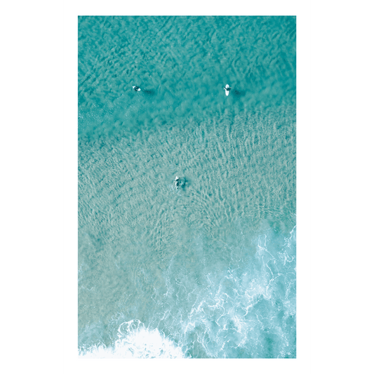 📸 An aerial view of Wamberal Beach, NSW, featuring three surfers in crystal-clear turquoise waters, with soft waves rolling onto the shore.
