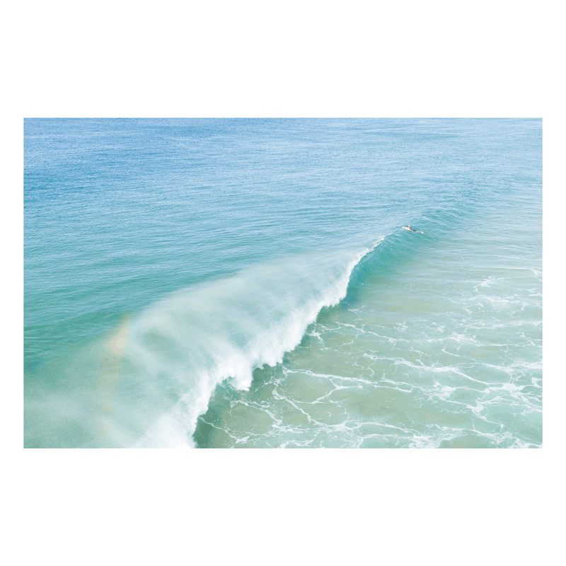 📸 An aerial view of a breaking wave at Wamberal Beach, NSW, with a soft rainbow appearing in the mist and pastel blue-green ocean hues.
