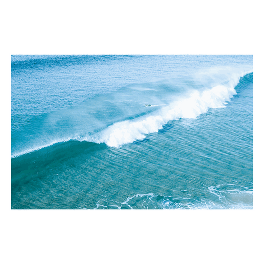 📸 An aerial view of a surfer duck-diving under a crashing wave at Wamberal Beach, NSW, with stunning aqua and deep blue ocean hues.
