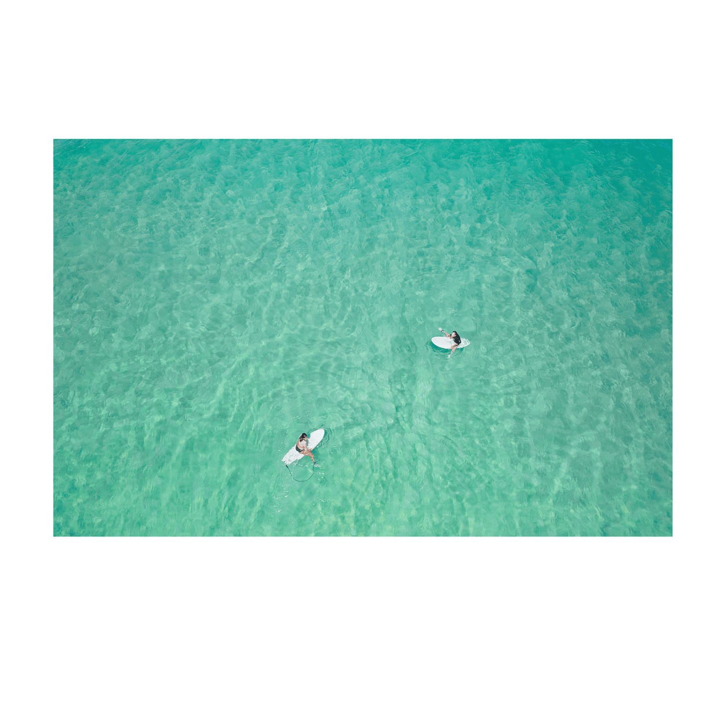 An aerial view of Wamberal Beach, NSW, showcasing two surfers floating in calm, crystal-clear turquoise waters.
