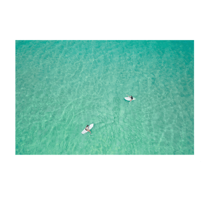 An aerial view of Wamberal Beach, NSW, showcasing two surfers floating in calm, crystal-clear turquoise waters.
